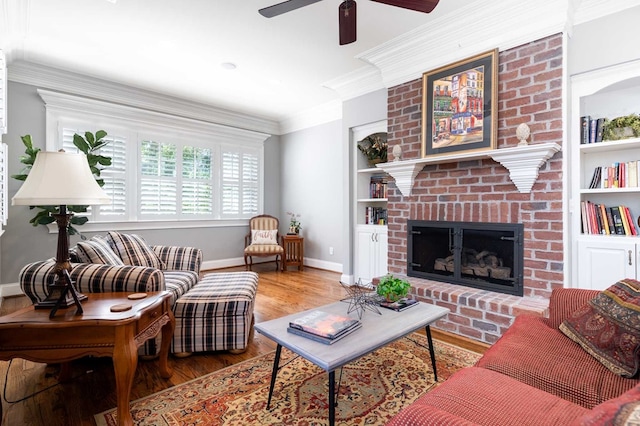 living room featuring a brick fireplace, built in shelves, ceiling fan, crown molding, and hardwood / wood-style floors