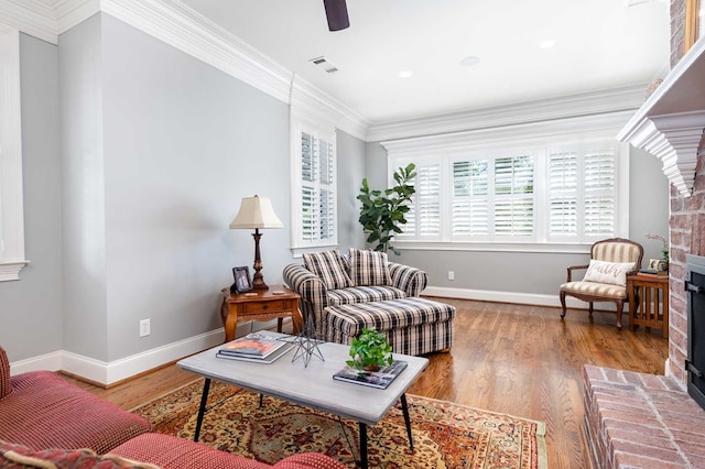 living room with hardwood / wood-style flooring, ceiling fan, ornamental molding, and a brick fireplace