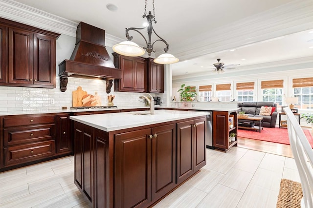 kitchen featuring a center island with sink, ceiling fan with notable chandelier, sink, hanging light fixtures, and custom range hood