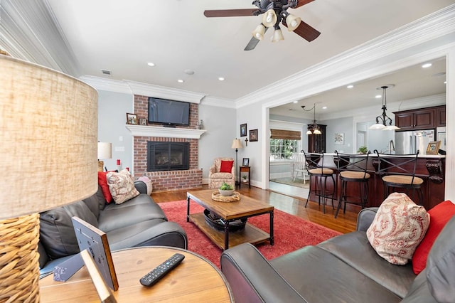 living room with hardwood / wood-style flooring, a brick fireplace, ceiling fan, and crown molding