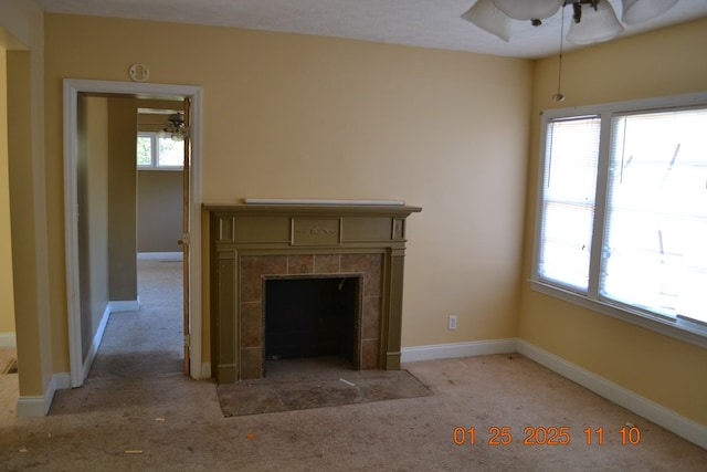 unfurnished living room featuring ceiling fan, a tiled fireplace, and light colored carpet