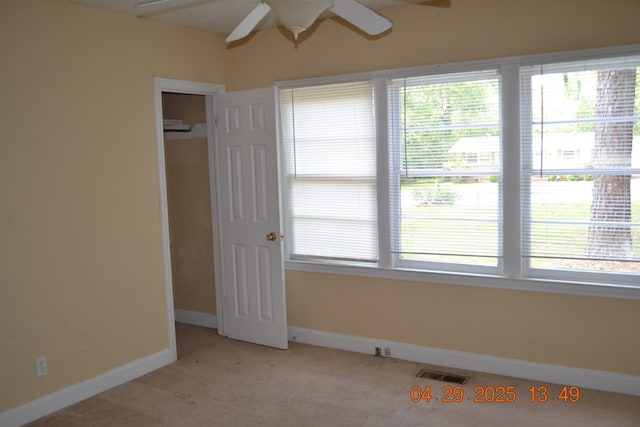 unfurnished room with a wealth of natural light, light carpet, a ceiling fan, and visible vents