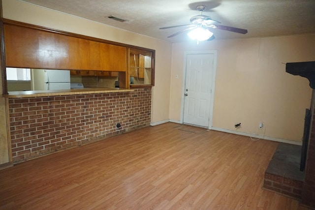 unfurnished living room featuring ceiling fan, brick wall, a textured ceiling, and light wood-type flooring