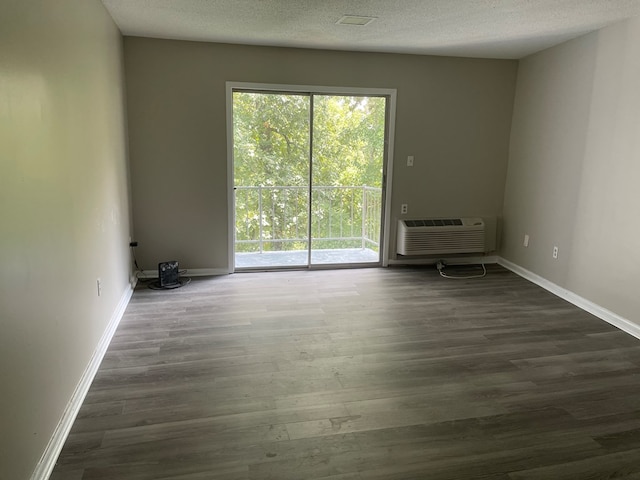 empty room featuring a wall mounted AC, dark wood-type flooring, and a textured ceiling