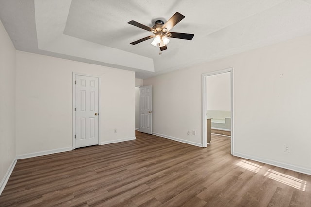 unfurnished bedroom with baseboards, a tray ceiling, and wood finished floors