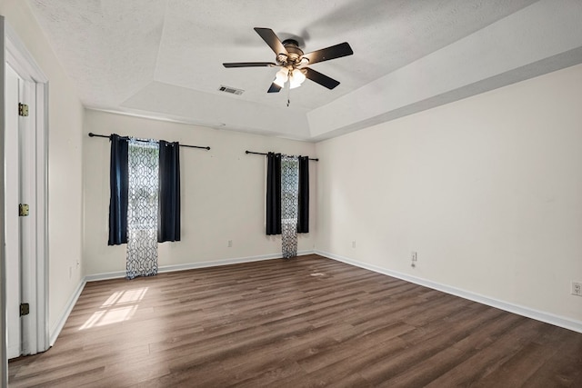 spare room with visible vents, wood finished floors, baseboards, ceiling fan, and a raised ceiling