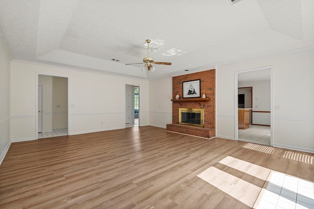 unfurnished living room with ceiling fan, a fireplace, light wood-style floors, baseboards, and a tray ceiling