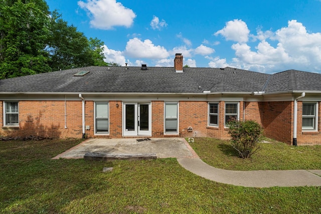 back of house featuring brick siding, a patio area, a lawn, and a chimney