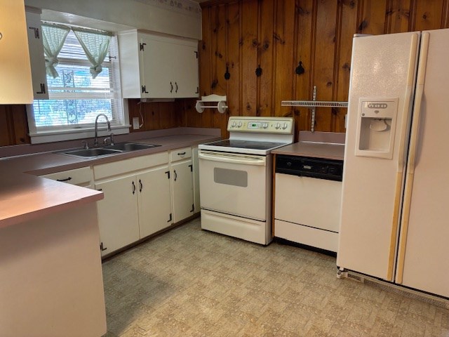 kitchen featuring sink, white appliances, white cabinetry, and wood walls