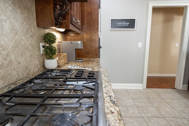 kitchen with light stone counters, light tile patterned floors, baseboards, gas stovetop, and tasteful backsplash