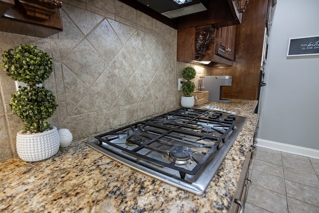 kitchen featuring backsplash, baseboards, light stone countertops, stainless steel gas cooktop, and light tile patterned flooring