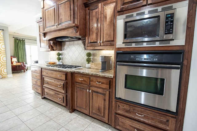 kitchen with tasteful backsplash, light tile patterned floors, stainless steel appliances, and light stone countertops