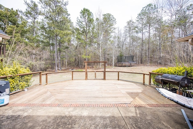 deck with grilling area, a forest view, and a trampoline