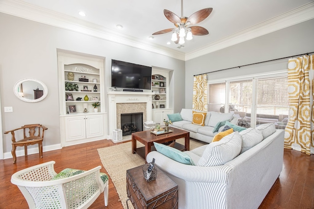 living area with built in shelves, wood finished floors, ceiling fan, and crown molding