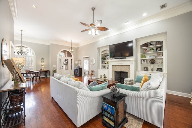 living area with visible vents, built in shelves, ceiling fan with notable chandelier, a fireplace, and dark wood-style floors