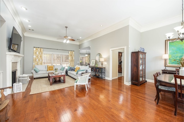 living room featuring crown molding, baseboards, ceiling fan with notable chandelier, a fireplace, and wood finished floors