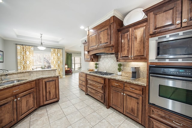 kitchen featuring a tray ceiling, ornamental molding, a sink, appliances with stainless steel finishes, and tasteful backsplash