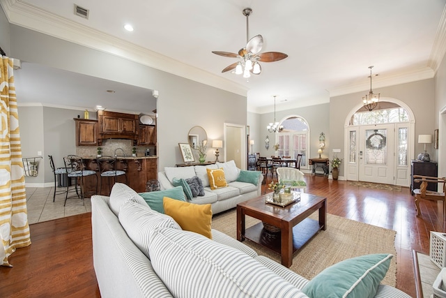 living room with baseboards, visible vents, ornamental molding, dark wood-type flooring, and ceiling fan with notable chandelier