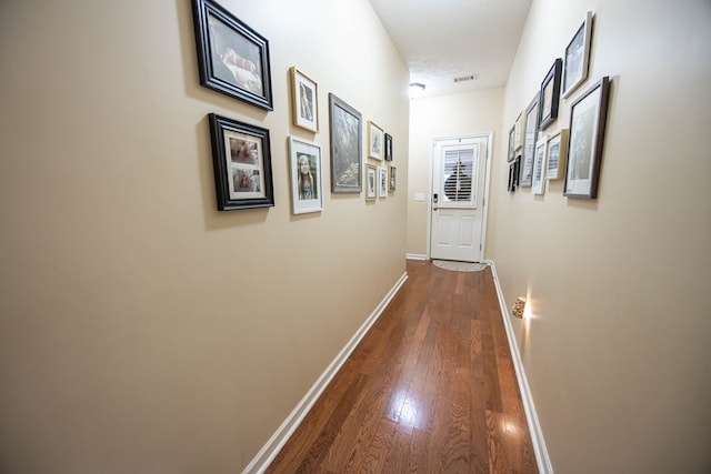 hall featuring visible vents, baseboards, and dark wood-style flooring