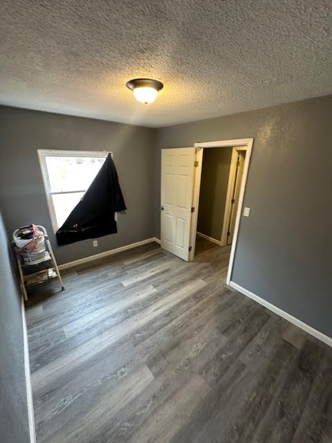 unfurnished bedroom featuring dark wood finished floors, a textured ceiling, and baseboards