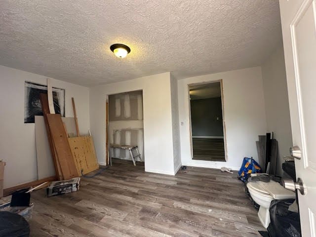 interior space with a textured ceiling, baseboards, and wood finished floors