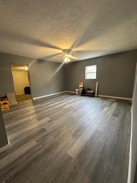 empty room with a textured ceiling, ceiling fan, dark wood-type flooring, and baseboards