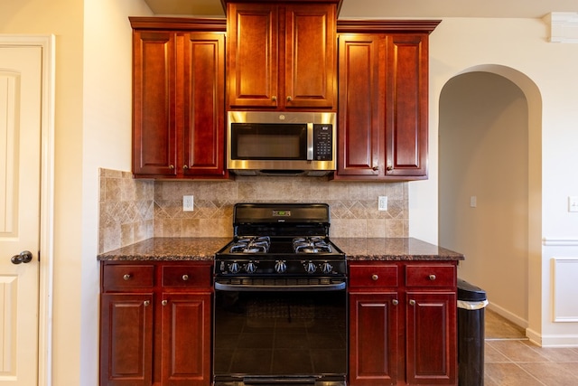 kitchen with light tile patterned flooring, black gas range oven, decorative backsplash, and dark stone countertops