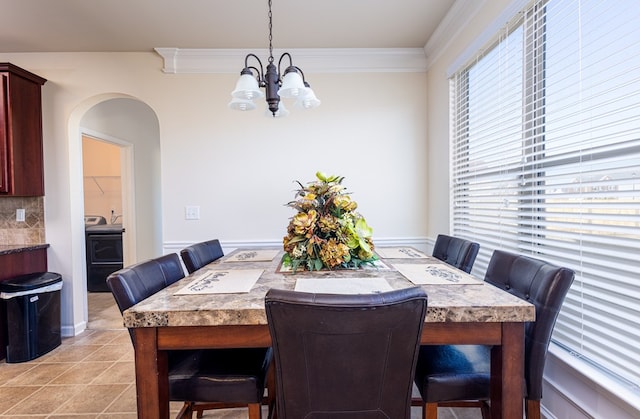 dining room featuring washer / dryer, light tile patterned floors, ornamental molding, and an inviting chandelier