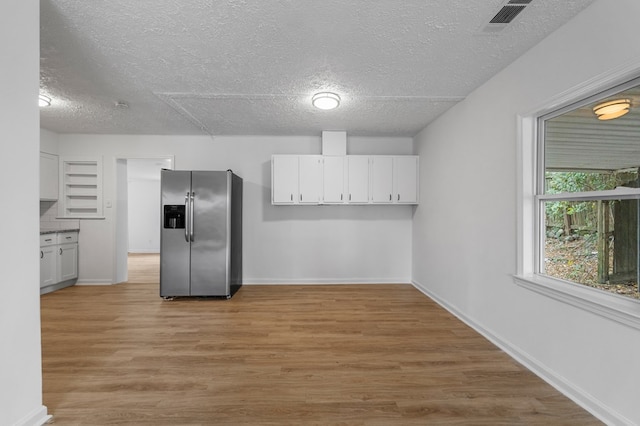 kitchen featuring stainless steel fridge, white cabinets, light hardwood / wood-style floors, and a textured ceiling