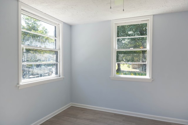 unfurnished room with a textured ceiling, a wealth of natural light, and dark hardwood / wood-style floors