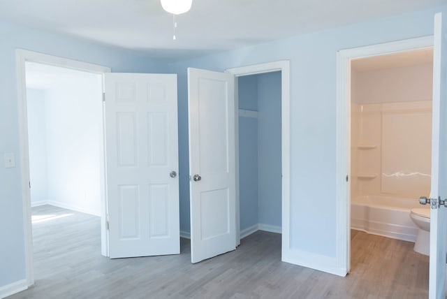 unfurnished bedroom featuring ensuite bathroom, a walk in closet, light wood-type flooring, and a closet