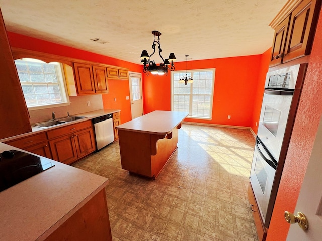 kitchen featuring sink, dishwasher, hanging light fixtures, a center island, and a chandelier