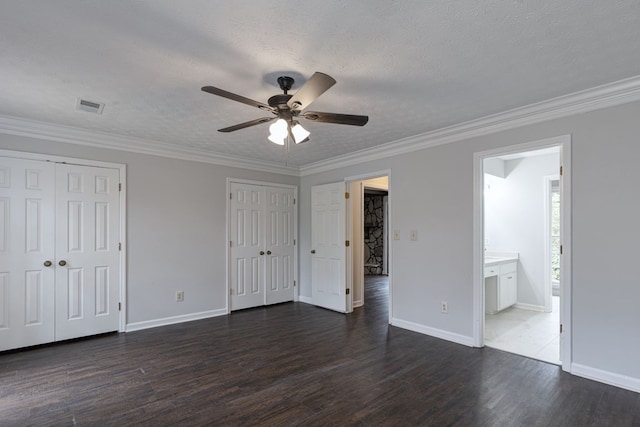 unfurnished bedroom with visible vents, crown molding, dark wood-type flooring, and multiple closets