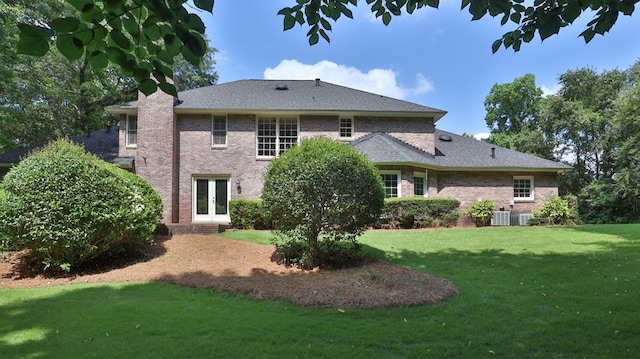 rear view of property featuring brick siding, french doors, a lawn, and a chimney