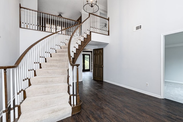 staircase featuring visible vents, baseboards, a high ceiling, wood finished floors, and a notable chandelier