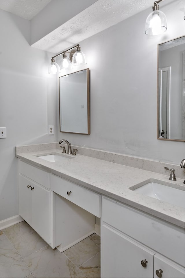 full bath with a sink, a textured ceiling, marble finish floor, and double vanity