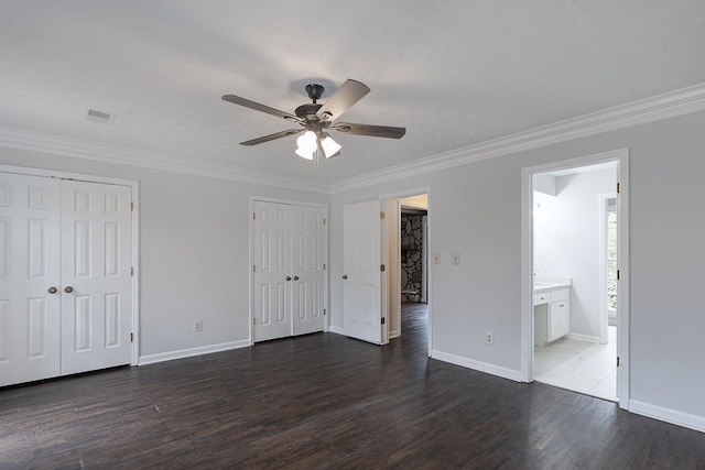 unfurnished bedroom featuring visible vents, two closets, dark wood finished floors, and crown molding