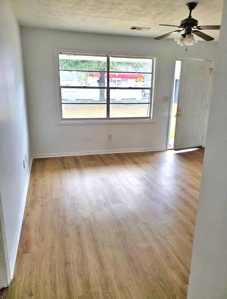 empty room with ceiling fan, plenty of natural light, a textured ceiling, and light wood-type flooring