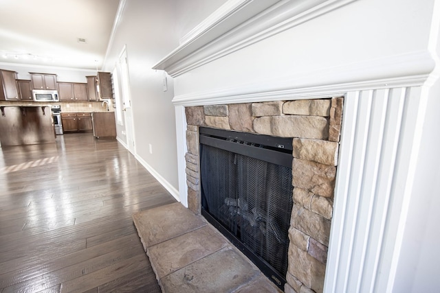 room details featuring a stone fireplace, stainless steel appliances, hardwood / wood-style flooring, ornamental molding, and decorative backsplash