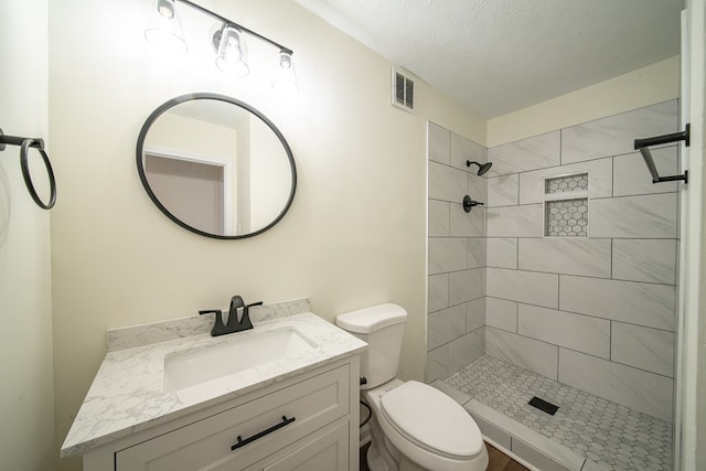 bathroom featuring a textured ceiling, vanity, toilet, and tiled shower