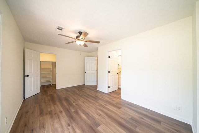 unfurnished bedroom with ceiling fan, a walk in closet, dark wood-type flooring, and a closet