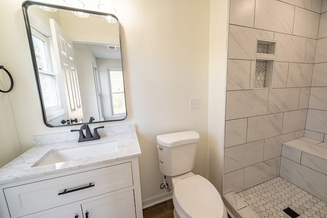 bathroom featuring tiled shower, vanity, and toilet