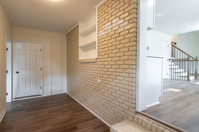 hall with crown molding, dark wood-type flooring, and brick wall