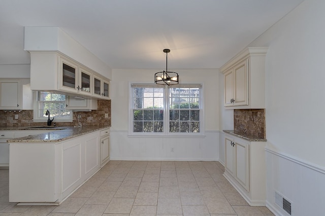 kitchen with a wainscoted wall, a sink, glass insert cabinets, and pendant lighting