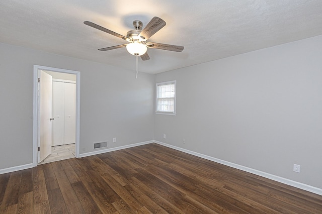 spare room featuring baseboards, visible vents, a ceiling fan, dark wood-type flooring, and a textured ceiling