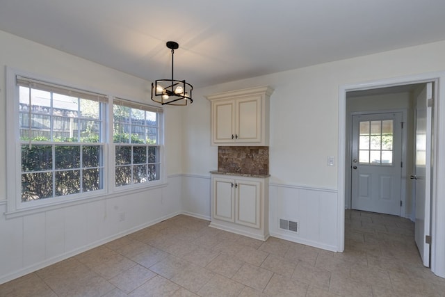 unfurnished dining area featuring a wainscoted wall, visible vents, and an inviting chandelier