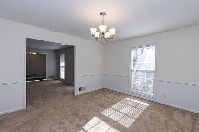 carpeted empty room featuring baseboards, visible vents, and a chandelier