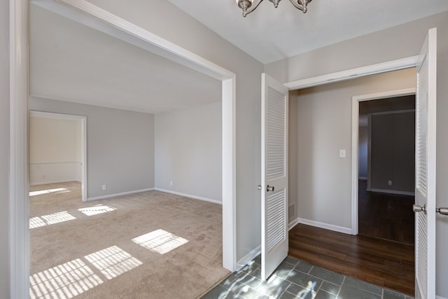 empty room with dark wood-style floors, a notable chandelier, and baseboards