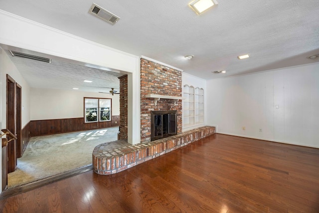 unfurnished living room featuring a fireplace, crown molding, a textured ceiling, and wooden walls