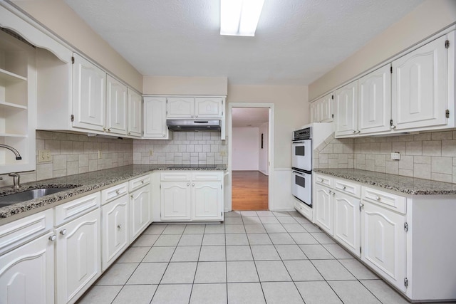 kitchen with light tile patterned floors, stone countertops, white cabinetry, and double oven